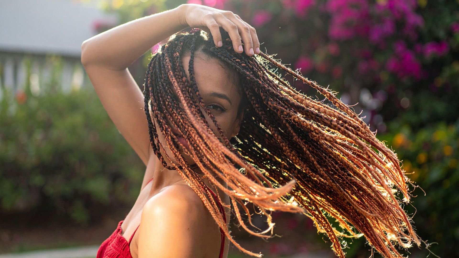 Woman with braids tossing hair in sunlight with colorful garden background